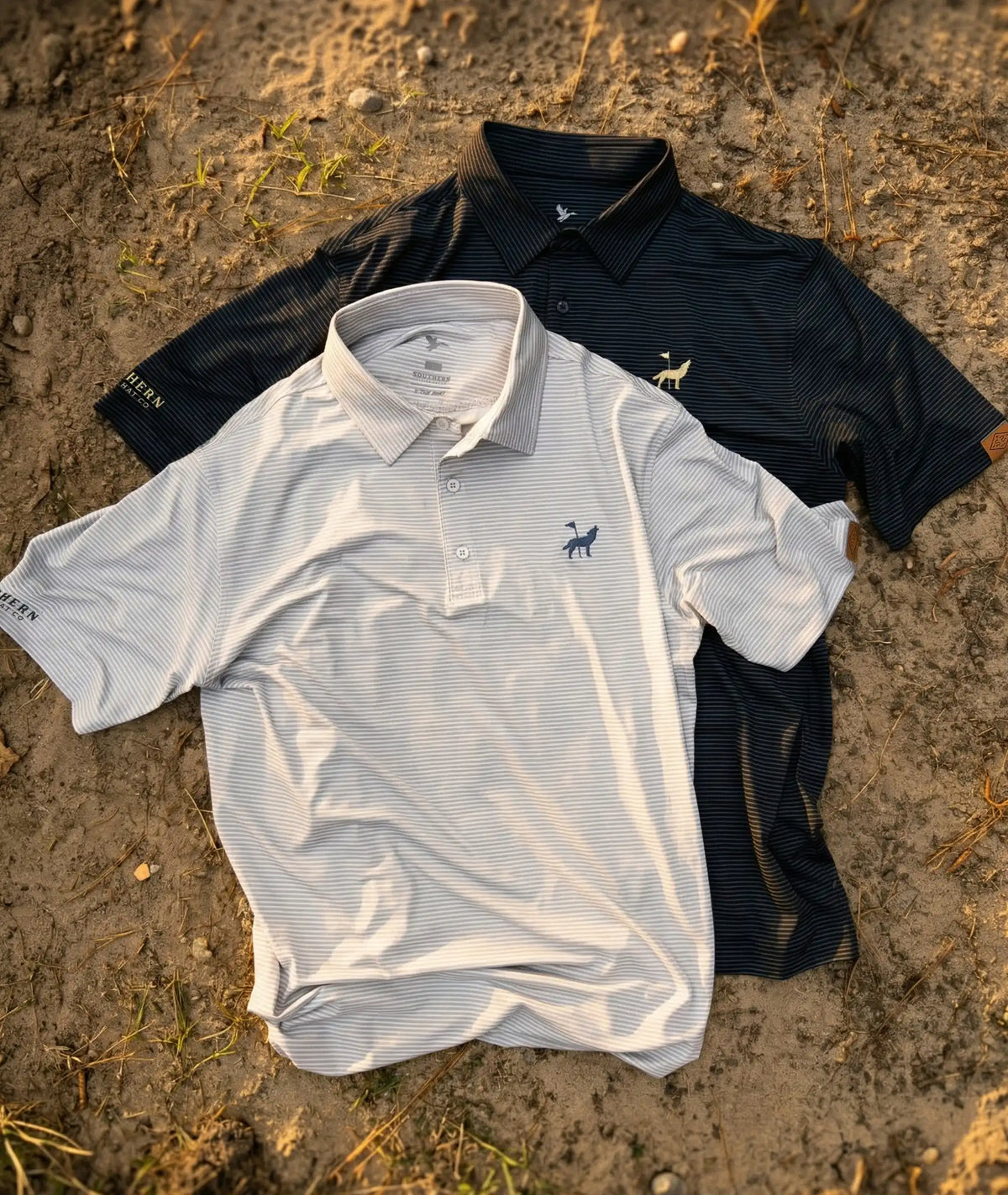 An overhead shot of Southern String Hat Co's American Jackal polo shirts featuring a white pinstripe and black pinstripe version with a small coyote golf embroidered logo on the chest and Southern String Hat Co logo on the sleeve