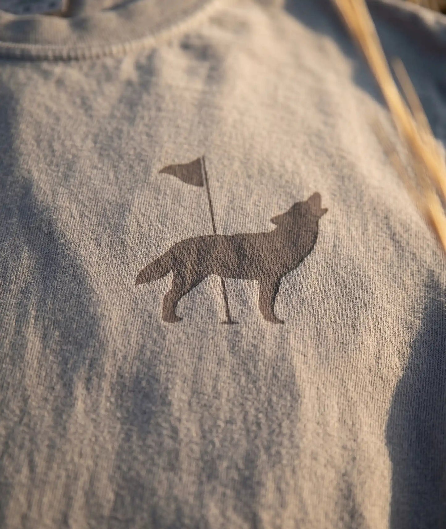 A close up macro shot of the front chest of Southern String Hat Co's 'The Howl' drop tee featuring a coyote and golf pin logo on a brown cinder colored tee