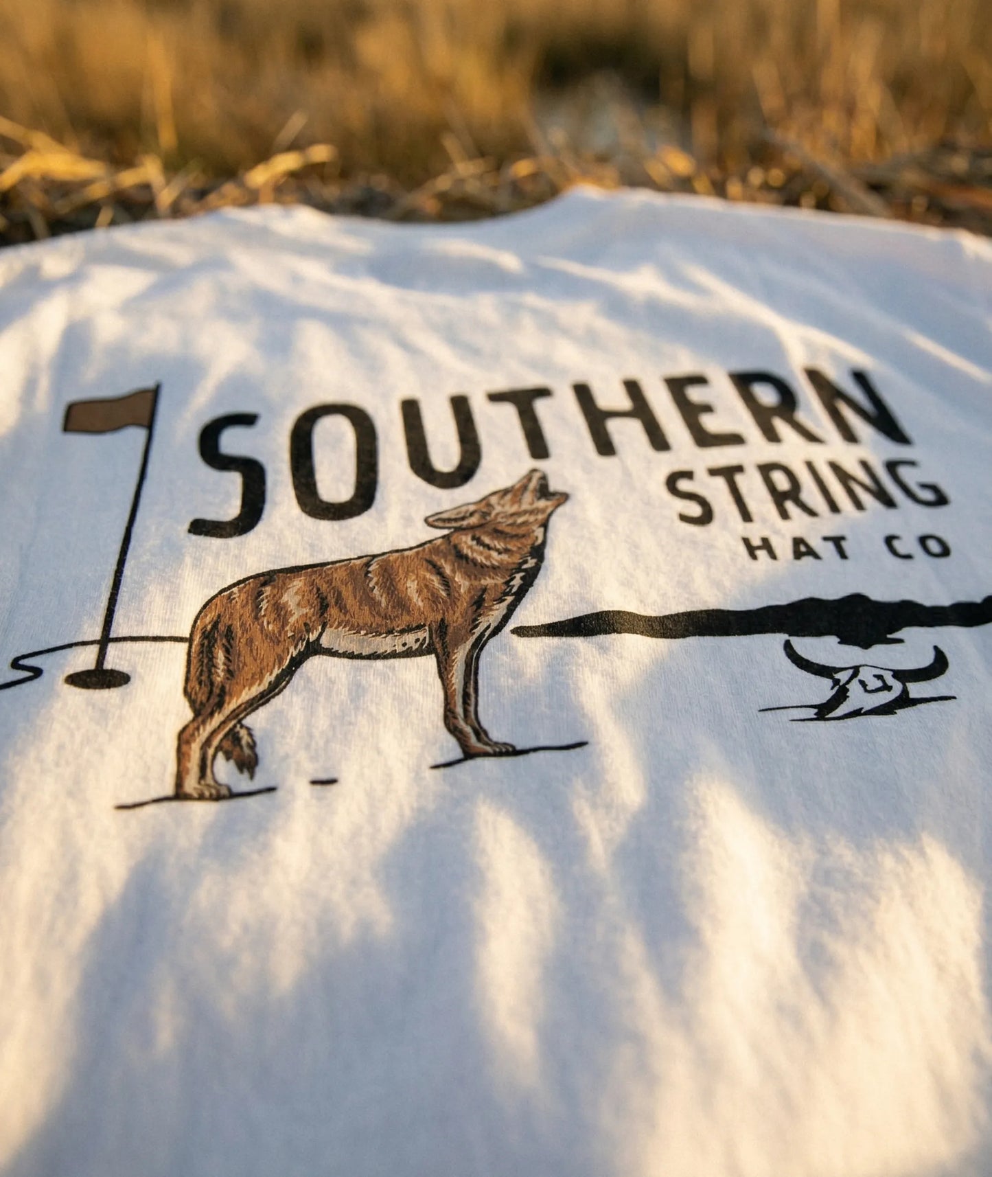 A close up macro shot of the back print of Southern String Hat Co's 'The Yote' drop t-shirt featuring a coyote and golf pin illustration on a white premium cotton tee